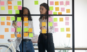 Image of two women creating a kanban board using sticky notes to depict "Simplifying Your Day-to-Day Operations"